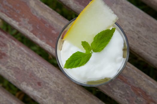 A glass of natural yogurt with a piece of melon, decorated by fresh leaves of peppermint. Top view