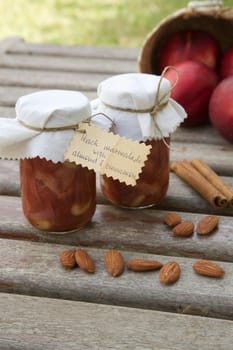 Homemade peach marmalade with almond nuts and cinnamon. Almonds,cinnamon sticks and fresh peaches in the background