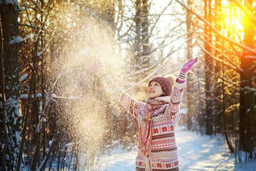 Portrait of the beautiful girl throwing snow in the winter wood