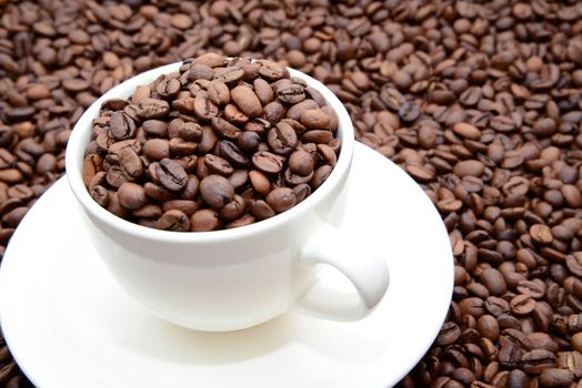 Photo of a cup of coffee with coffee grains on a saucer. White color cup on a brown coffee beans background. Food photography.