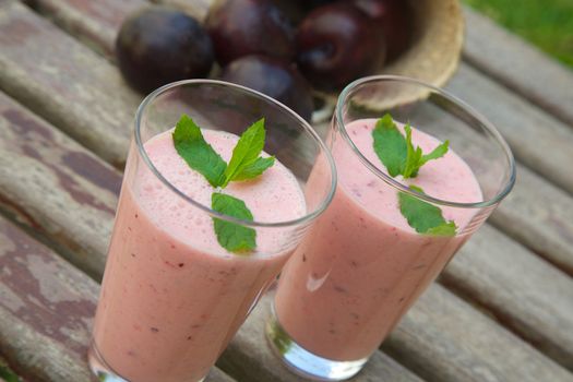 Two glasses of plum smoothie  with fresh peppermint leaves. Fresh plums in the background