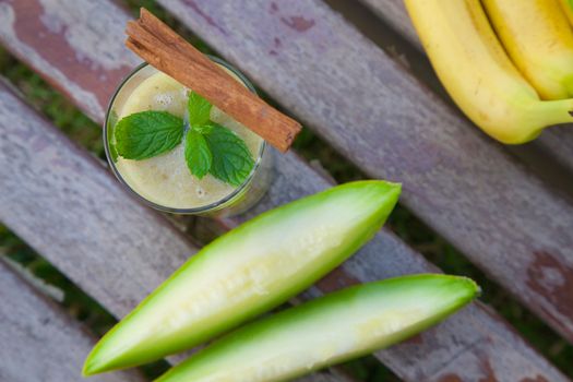A glass of banana-melon smoothie with fresh peppermint leaves and cinnamon steaks. Top view