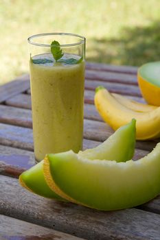 A glass of banana-melon smoothie. Fresh bananas and green melon in the background
