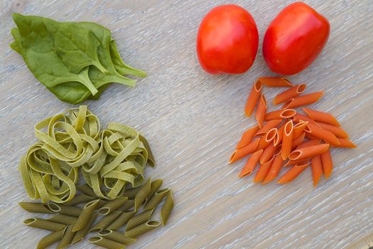 Colorful Italian dried pasta and its compounds.Spinach and tomato pasta on the wooden surface