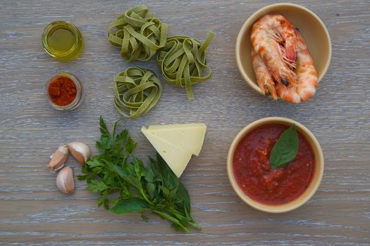 Food ingredients for preparing pasta with shrimps on the wooden surface