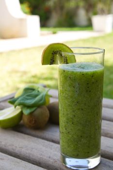 Spinach-kiwi-green apple smoothie in the glass. Kiwi, spinach leaves, green apple and lemon in the background