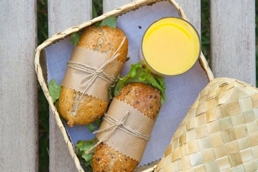 An open-air  express lunch for a vegetarian- whole grain rolls with fresh vegetables and a glass of fresh orange juice. Rolls are hidden in the woven birch basket
