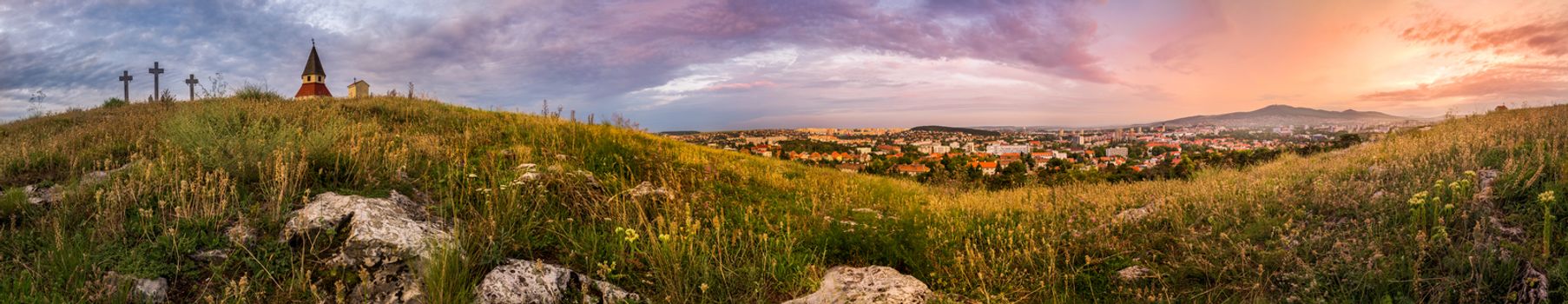 City and Village under a Hill at Sunset as Seen from Calvary, Nitra, Slovakia. Meadow with Flowers and Rocks in Foreground.