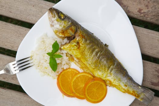 Vegetarian lunch - baked sea bass in an orange sauce and rice. The dish is place on an old wooden surface.