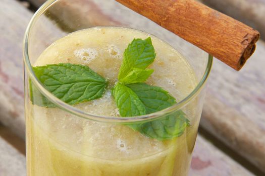 A glass of banana-melon smoothie with fresh peppermint leaves and cinnamon sticks. Close up