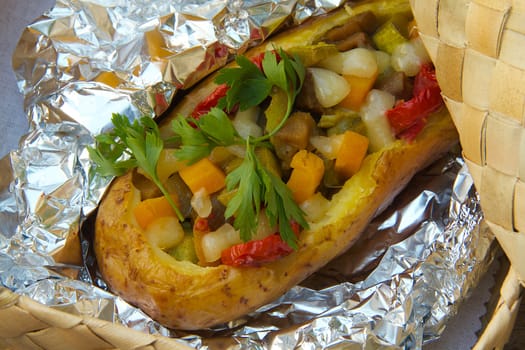 Open-air lunch for a vegetarian- potato baked with vegetables and cheese in an aluminium foil. Dish is hidden in the woven birch basket