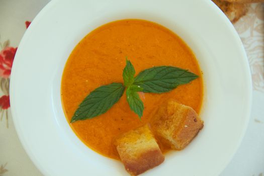 Light lunch soup-tomato soup with croutons in white plate on a flower print table cloth