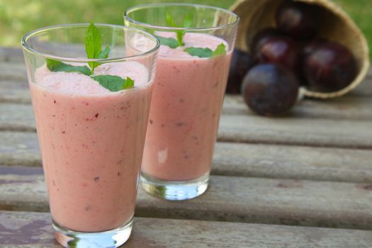 Two glasses of plum smoothie  with fresh peppermint leaves. Fresh plums in the background