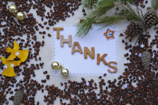 Winter holidays cedar nuts background on a wooden surface with  biscuits inscription:"Thanks"