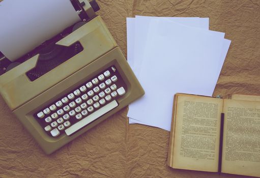 Typing machine, white sheets of paper,old book on an old paper surface. Top view. Free space for a text