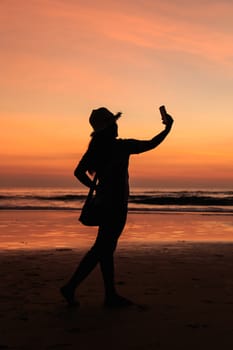 Silhouette of Thai Woman using smartphone at the beach in sunset time