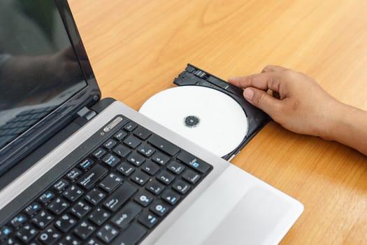Hand inserting a cd on laptop on table