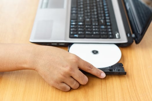 Hand inserting a cd on laptop on table