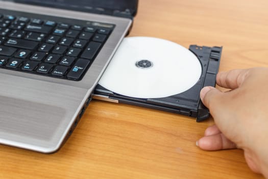 Hand inserting a cd on laptop on table