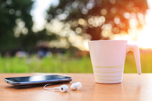 Coffee cup and smartphone on the table in sunset time