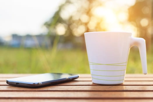 Coffee cup and smartphone on the table in sunset time