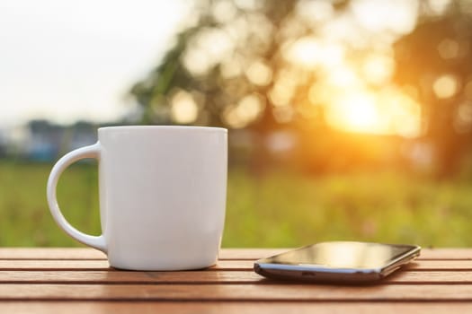 Coffee cup and smartphone on the table in sunset time