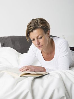 Adult woman with short hair reading a book in bed