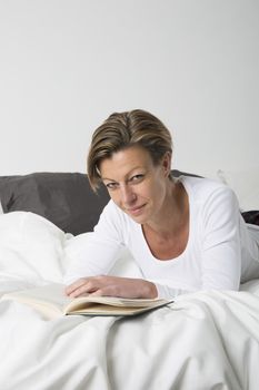 Smiling woman with short hair reading a book in bed