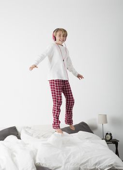 Smiling Little Girl with headphones jumping in bed