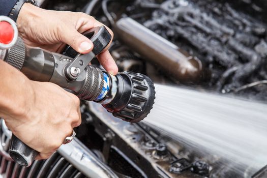 Hand holding water hose to prevent fire on car