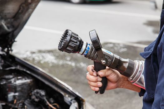 Hand holding water hose to prevent fire on car