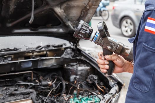 Hand holding water hose to prevent fire on car