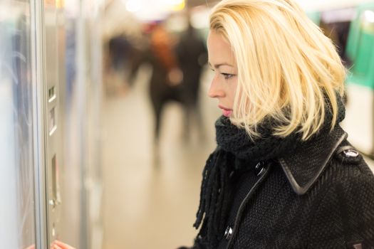 Casually dressed woman wearing winter coat,buying metro ticket at the ticket vending machine. Urban transport.