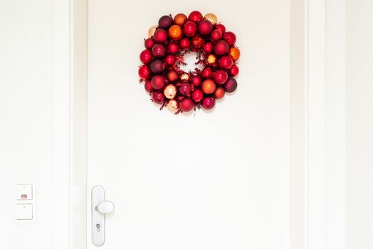 Christmas wreath decorated with red balls on white entrance door to a flat
