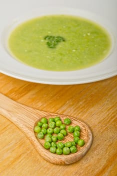 Fresh green pea soup in white soup plate. With wooden spoon full of green pea.