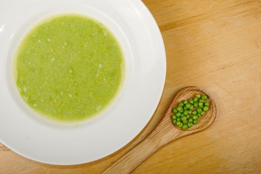 Fresh green pea soup in white soup plate. With wooden spoon full of green pea.