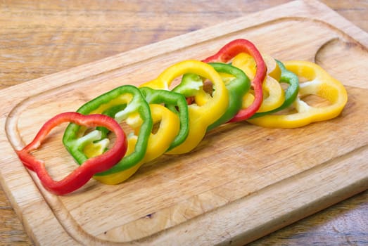 Tricolored  sweet pepper slices on the wooden plate