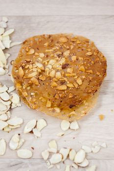 Almond lace cookies with slivered almonds on a wooden counter top.