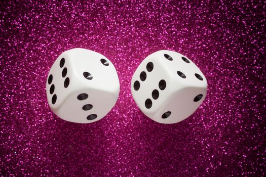 Rolling white dice over purple glittering surface