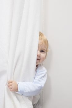blonde baby sixteen month old peeking face behind white curtain