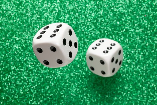 Rolling white dice over green glittering surface