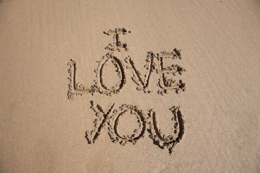 i love you text written on brown sand ground low tide beach ocean seashore in Spain Europe