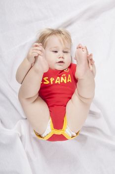 blonde baby sixteen month old with red shirt of Spanish soccer team lying with legs up