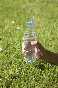 transparent small plastic water bottle with blue cap in woman hand on green lawn outdoor