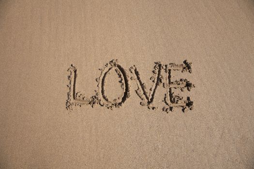 love word written on brown sand ground low tide beach ocean seashore in Spain Europe