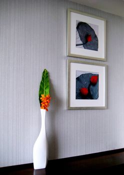A white vase beside red lotus pictures on the white wall. It is like a peaceful place.