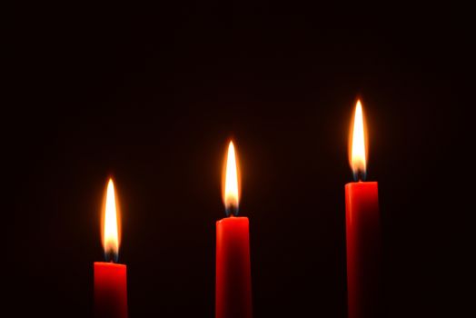 Photo of three red candles on a black background. Object photography.