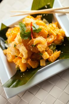 Thai crispy shrimp dish with apple and sesame seeds presented beautifully on a white square plate with chopsticks.