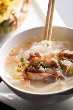 Closeup of a person eating Thai style crispy pork rice noodle soup from a bowl with chopsticks. Pineapple fried rice in the background.