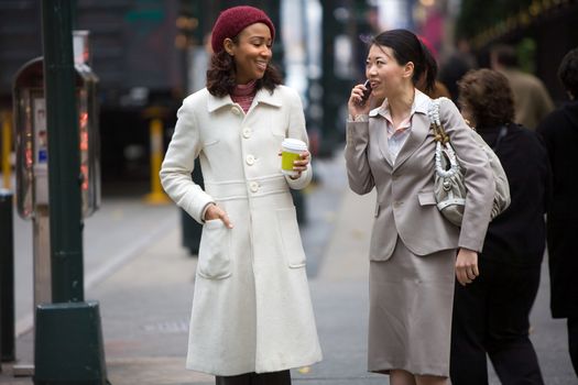 Two business women walking in the big city. One is on her cell phone.